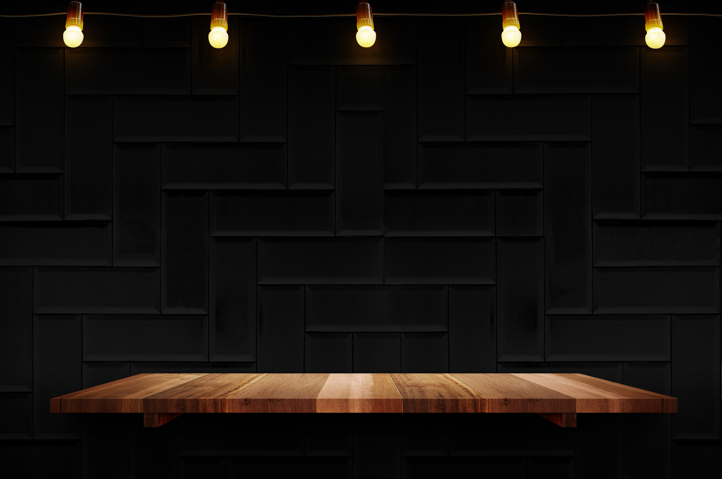 Empty brown plank wood shelf at black modern tile wall background with light bulbs string,Mockup for display or montage of product or design.